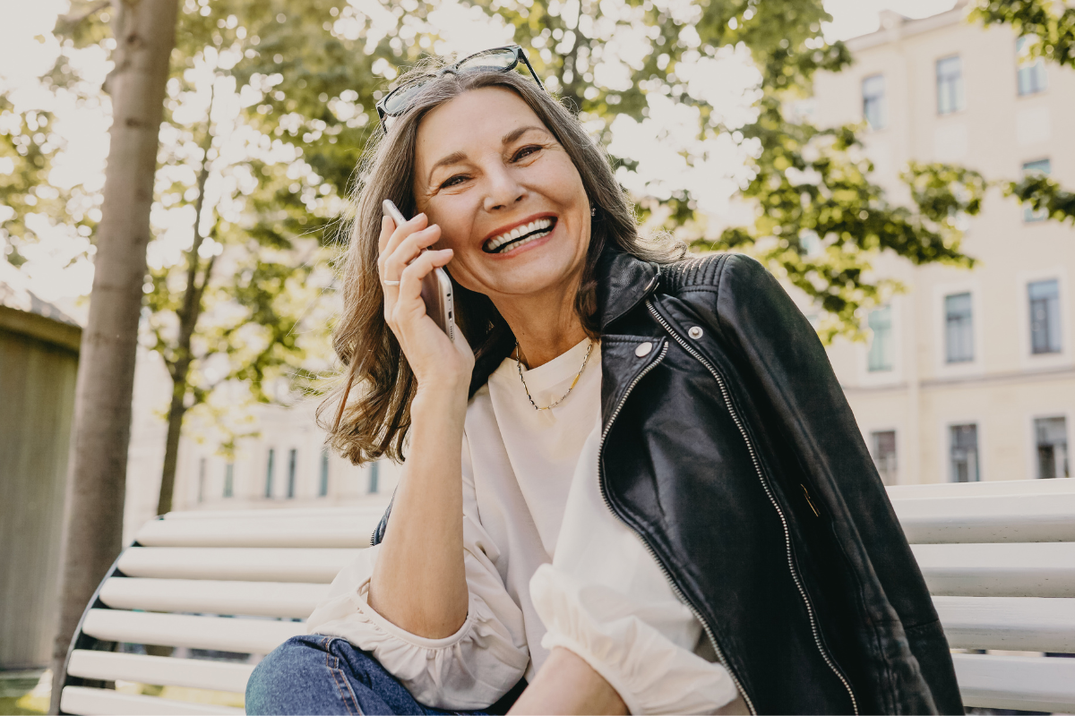 older woman leather jacket on bench on cell phone