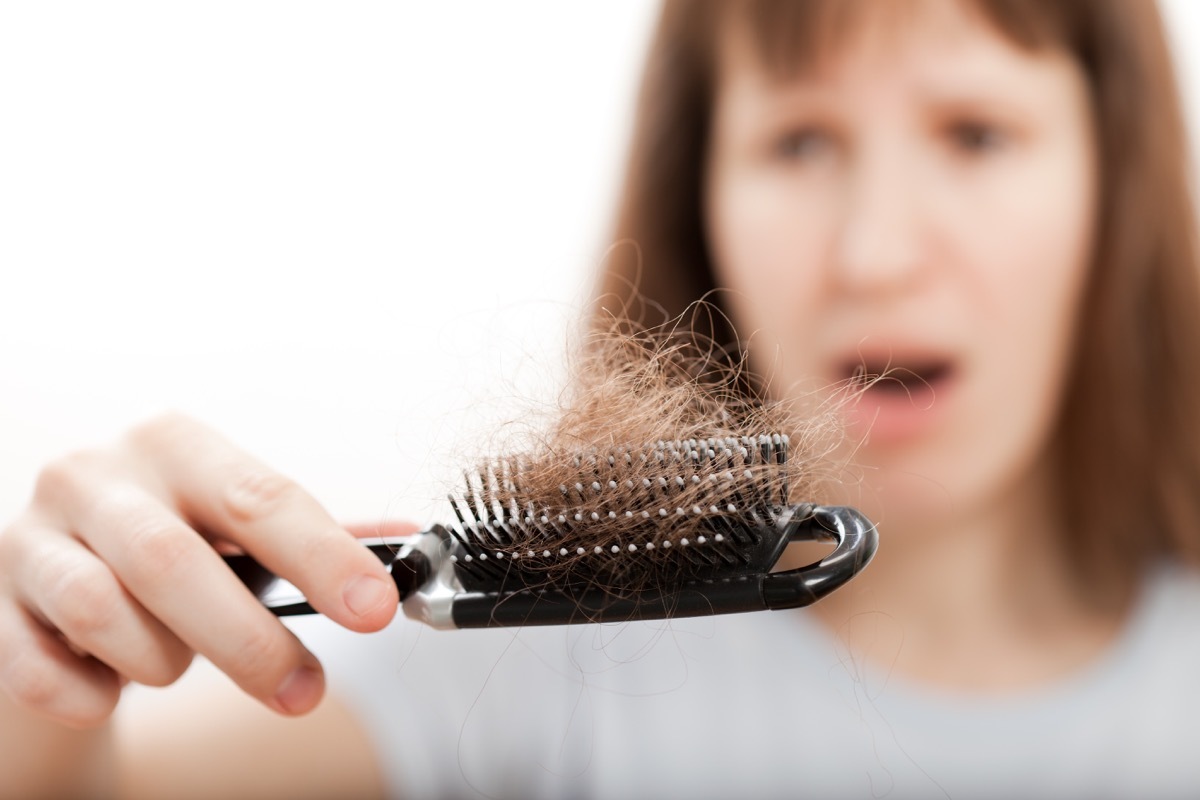 woman looking in shock at hair in her comb signs your metabolism is slow