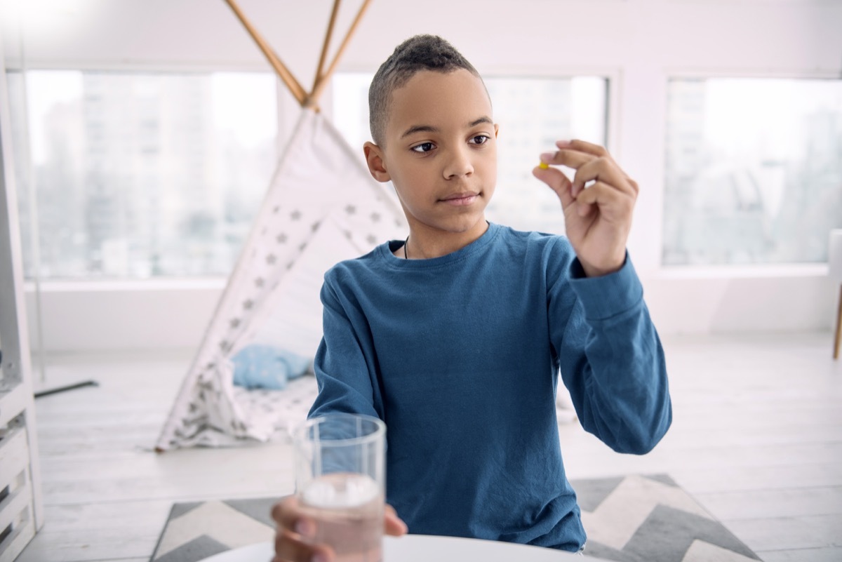 teen staring at pill while holding glass of water