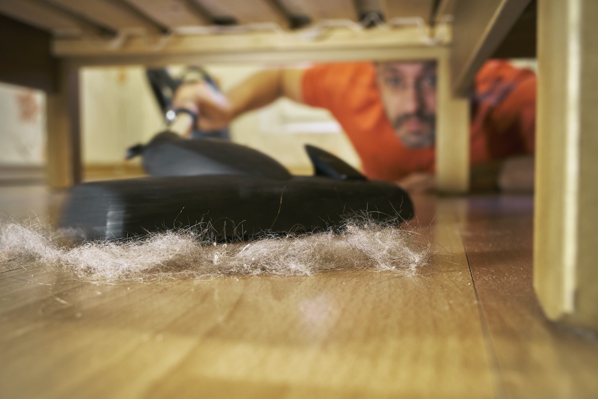 person vacuuming pet hair under sofa