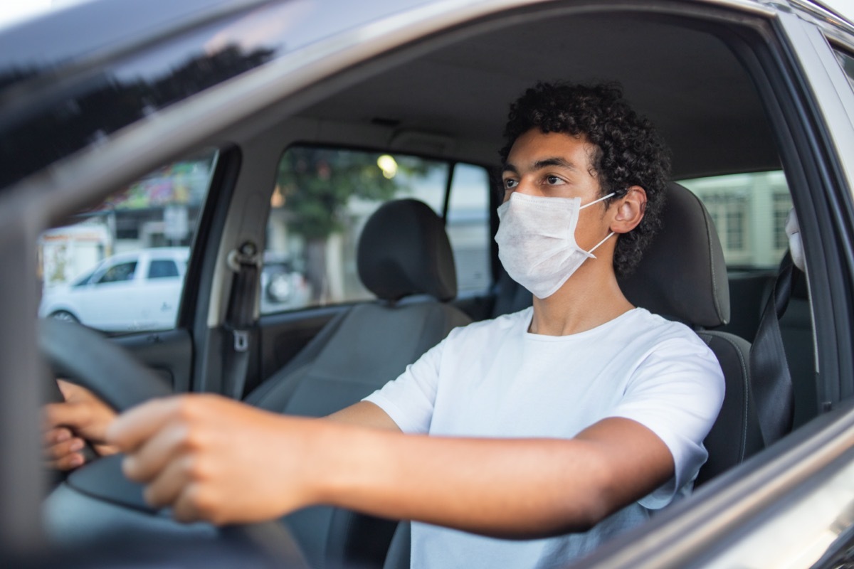 man with protective mask inside the car with his hands on the steering wheel looking forward