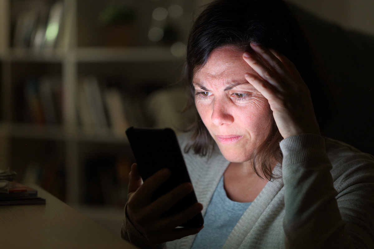 Woman reading on smart phone lighted screen sitting at night at home