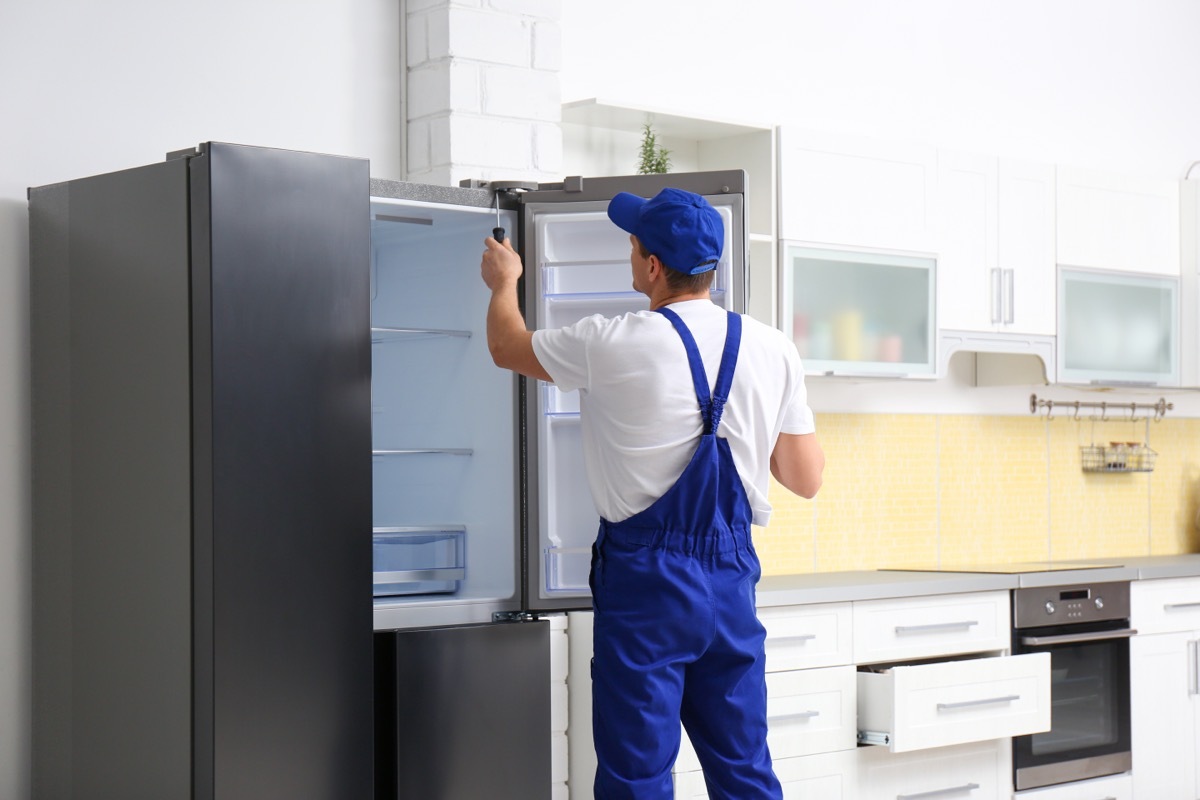 Male technician with screwdriver repairing refrigerator in kitchen