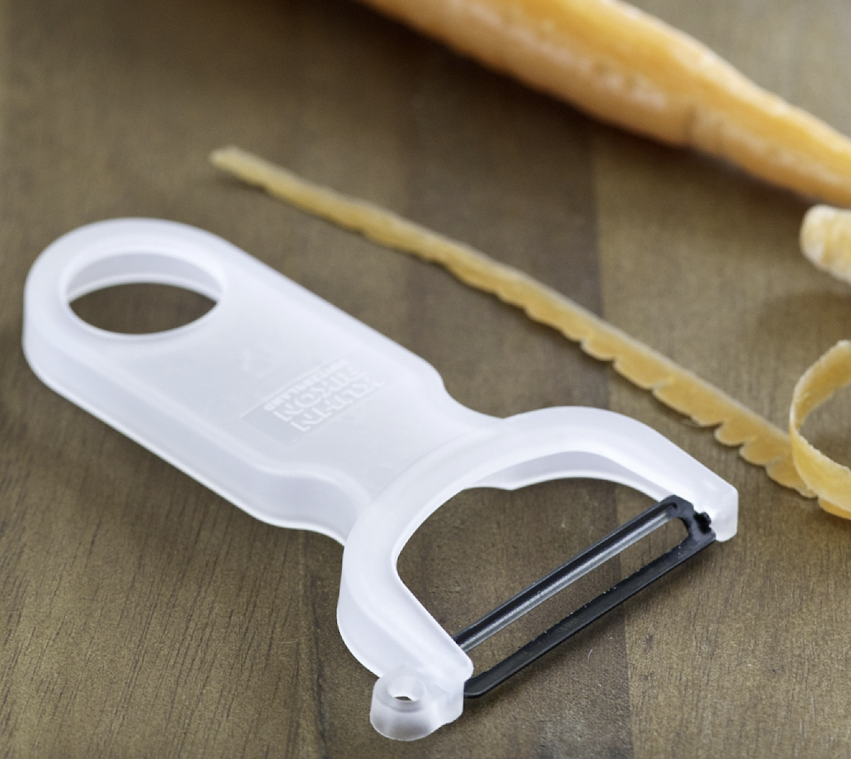 A white peeler on a wood background next to a carrot