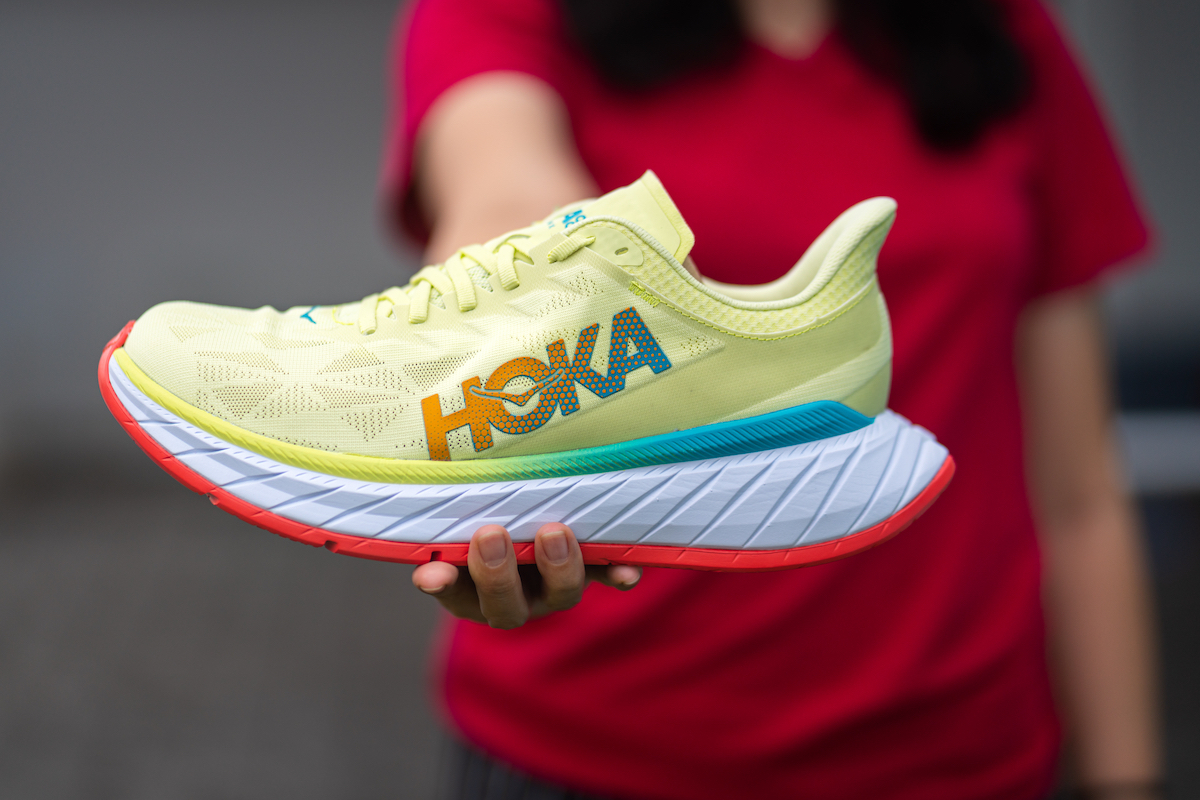 Blurred woman in a red shirt holding a pale yellow Hoka sneaker