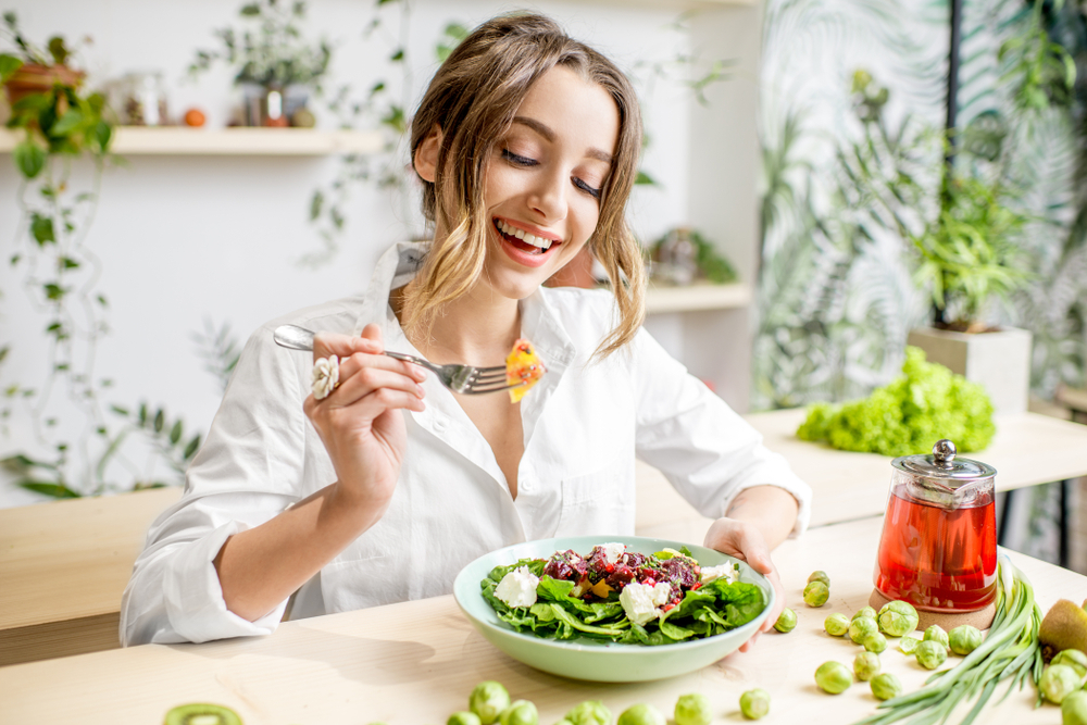 A young woman eating a salad at a kitchen table