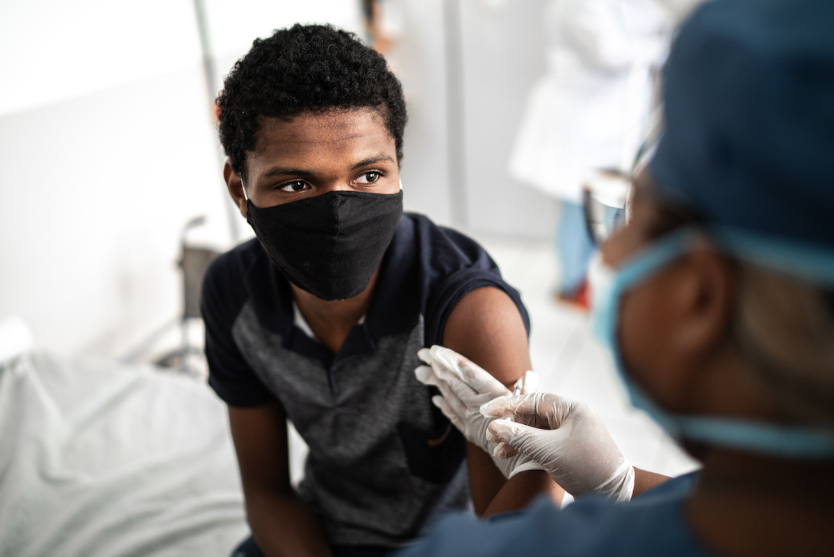 Doctor vaccinating teenage boy wearing face mask