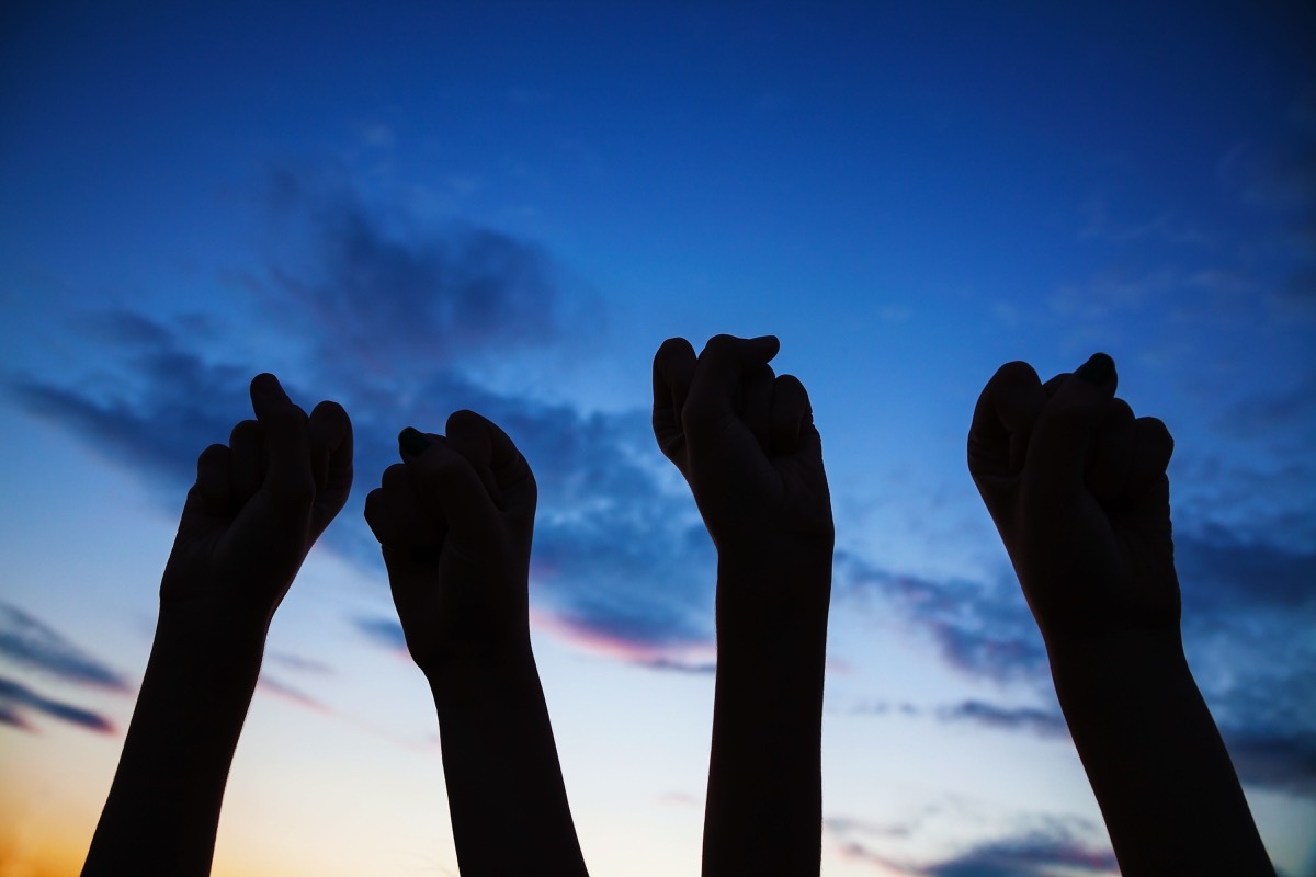 Clenched fists raised high in protest for rights D3AHT7 Four clenched fists raised against blue sky