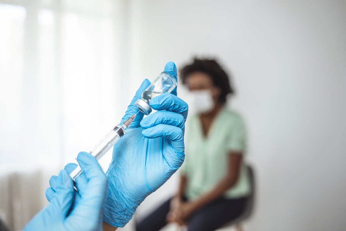 Doctor's hands in surgical gloves preparing COVID-19 vaccine for female patient. Female doctor pulling COVID-19 vaccine liquid out from vial with syringe. Prevention and immunization from corona virus infection