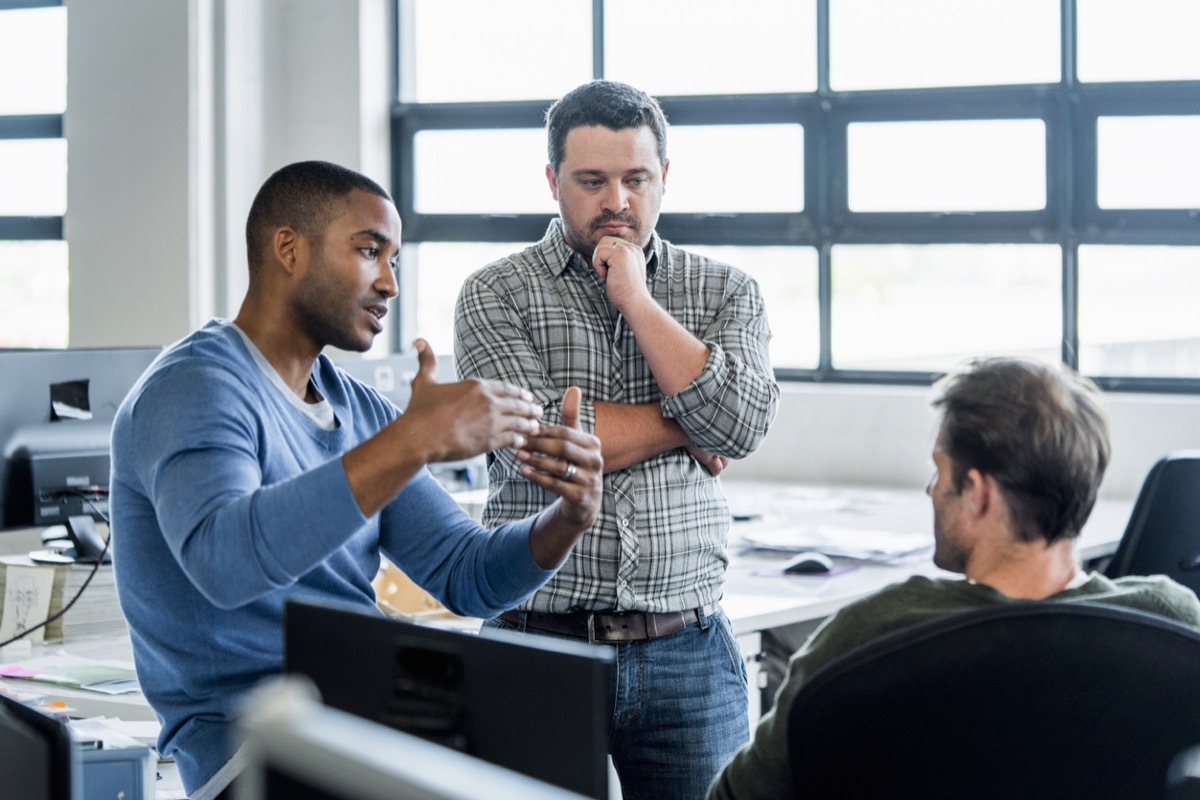 three men sitting around an office having a conversation