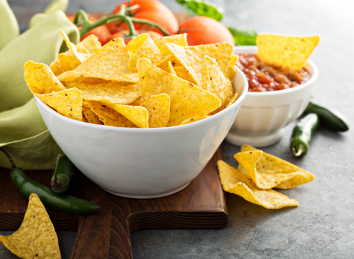 Yellow corn tortilla chips with a bowl of salsa on a cutting board