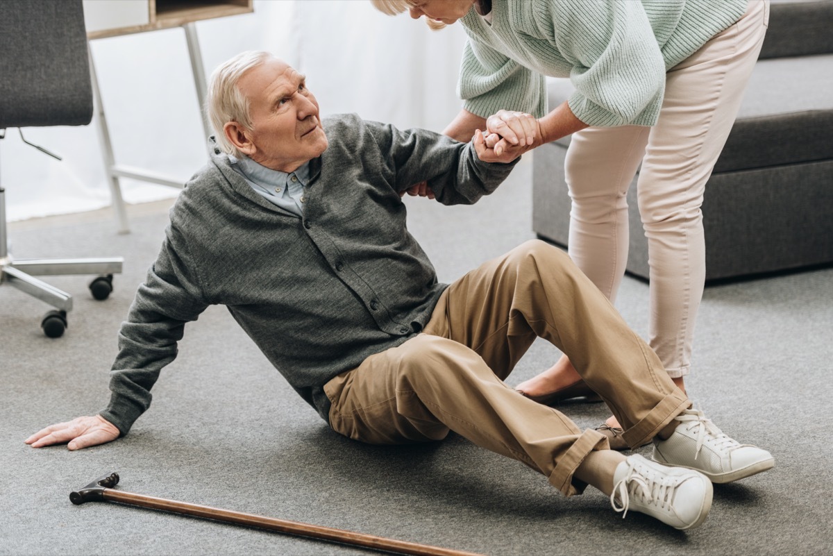 woman helping to stand up husband who falled down on floor near walking stick