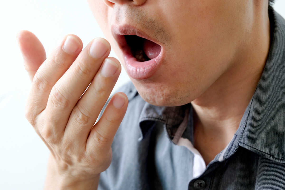 young man checks for bad breath by holding hand out in front of mouth and breathing