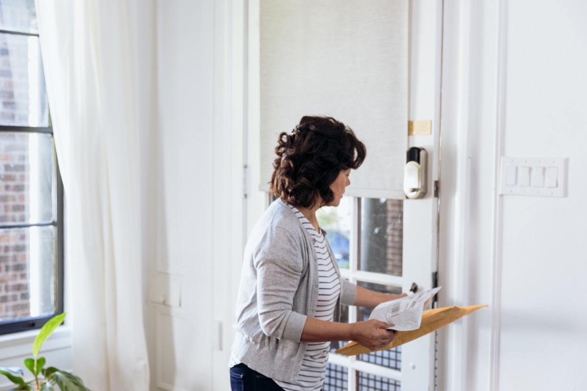 Senior woman closes the front door after picking up a package from the porch.