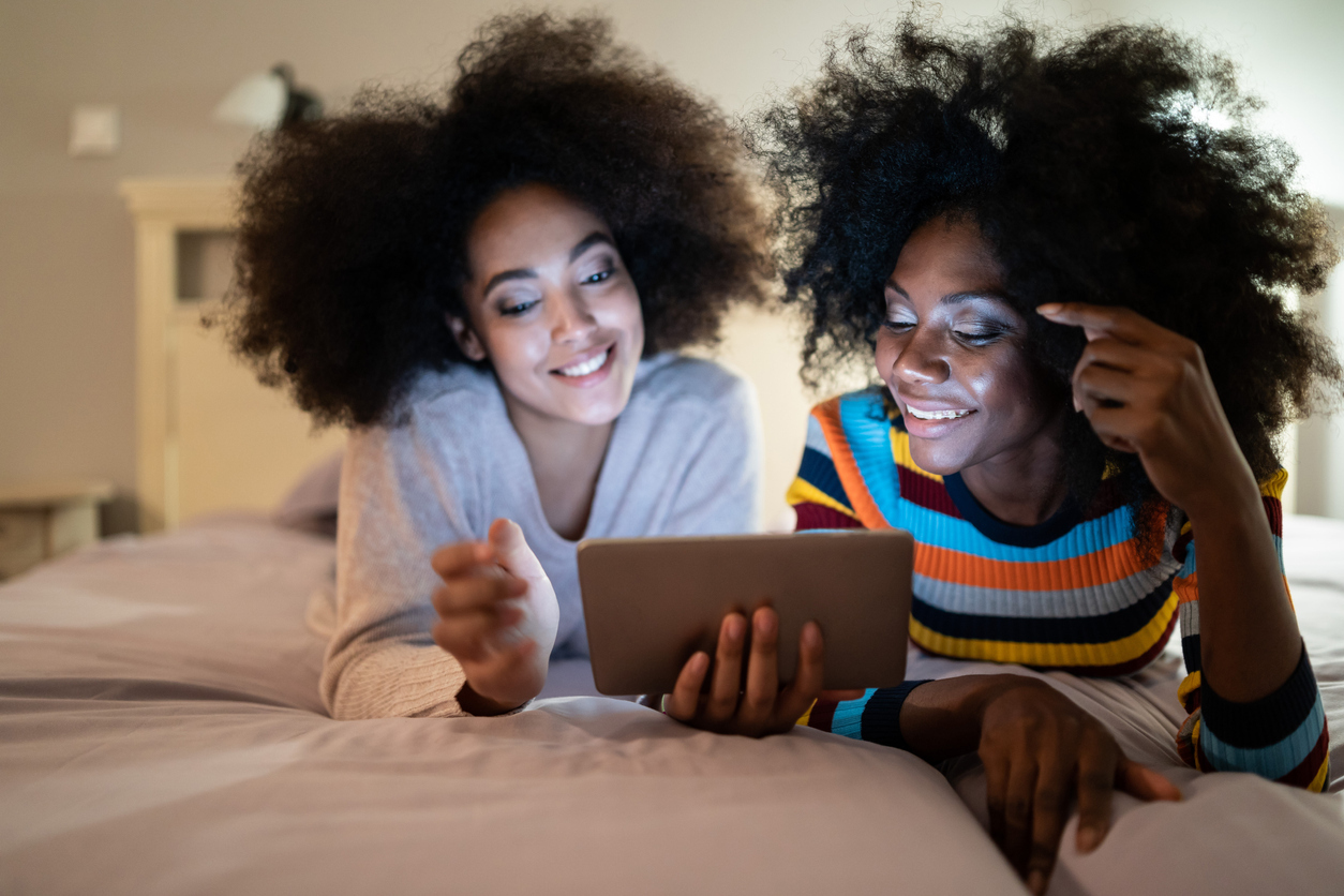 Friends using digital tablet in bed