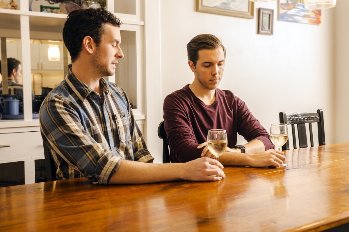 male gay couple sitting at a dining table with serious looks on their faces.. Real people. Real couple.