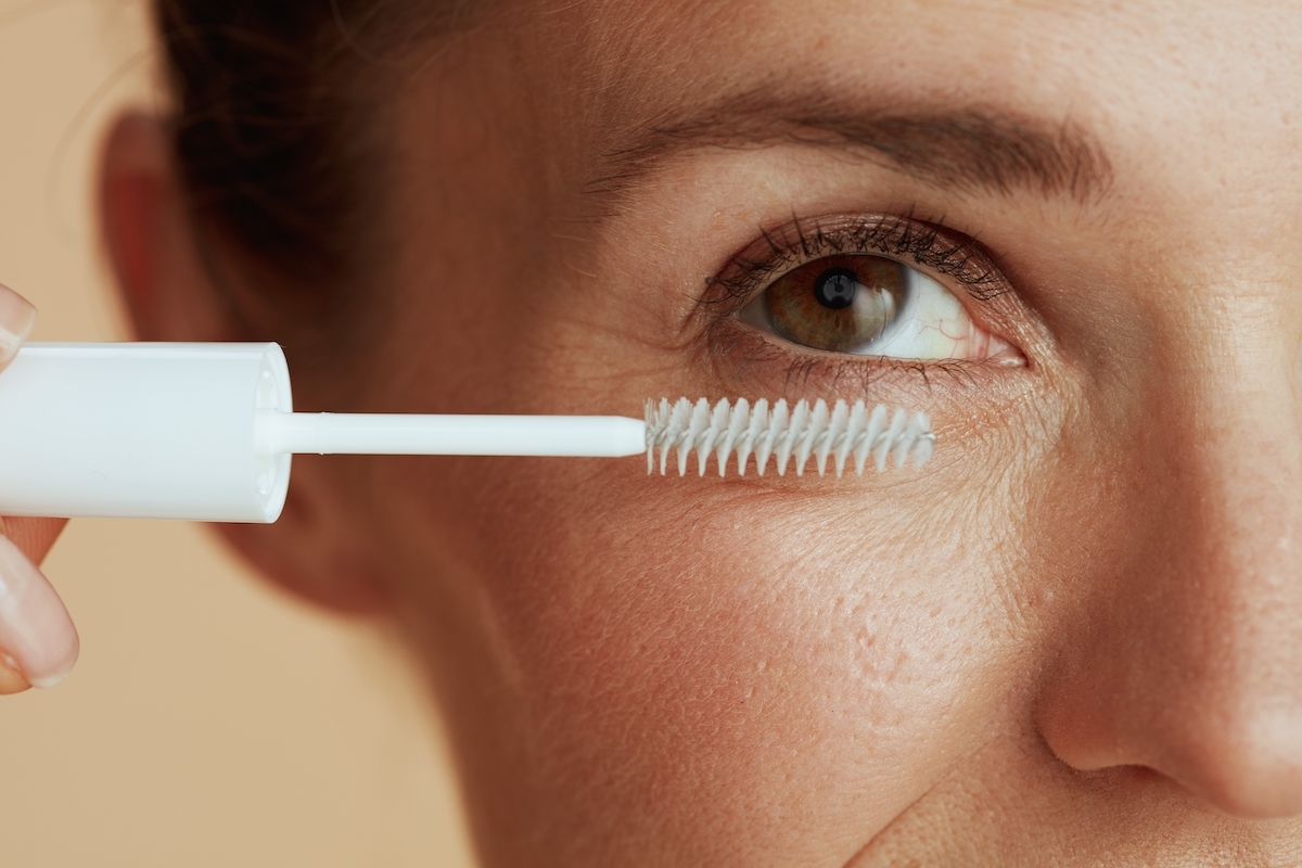 Close up of a woman applying a clear mascara gel in a white tube to her eyelashes