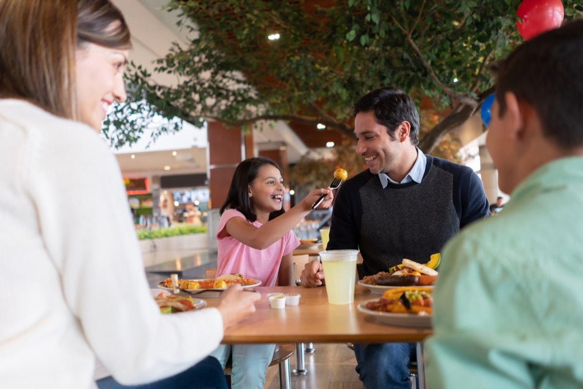 Happy girl eating luch with her family and sharing food with her father while smiling - lifestyle concepts