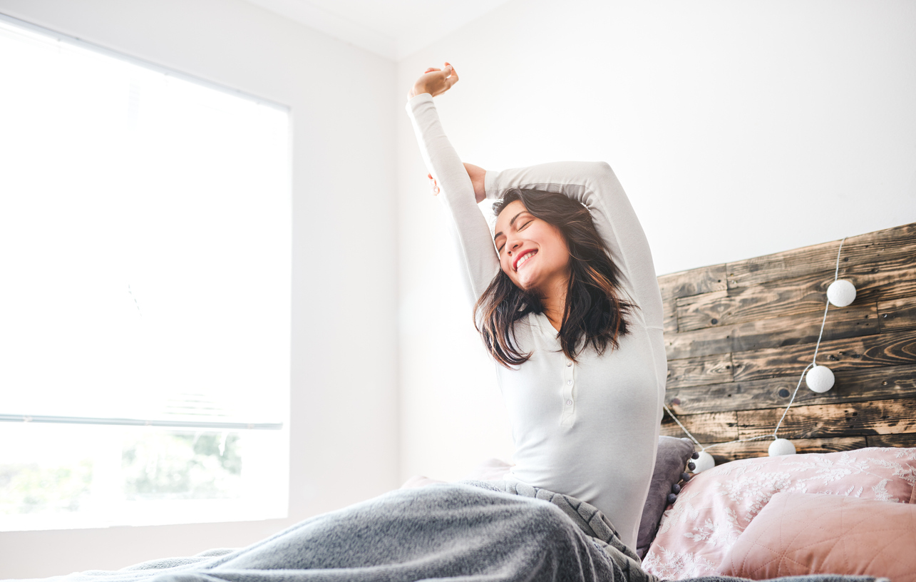 Cropped shot of a young woman stretching while sitting in her bed