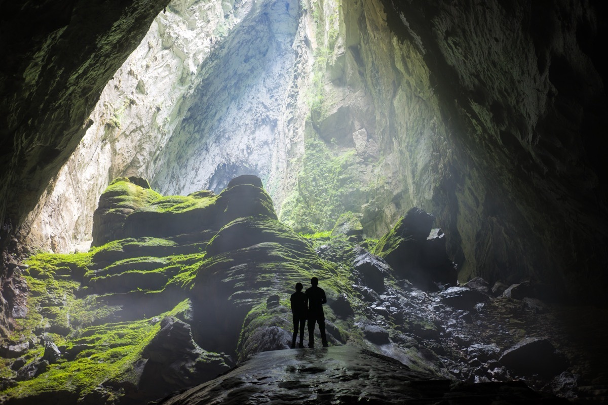 the backs of two people standing in a huge cave