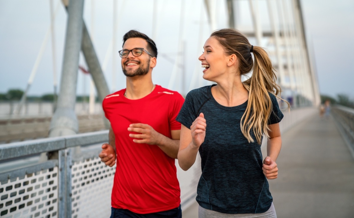 man and woman jogging together across a bridge