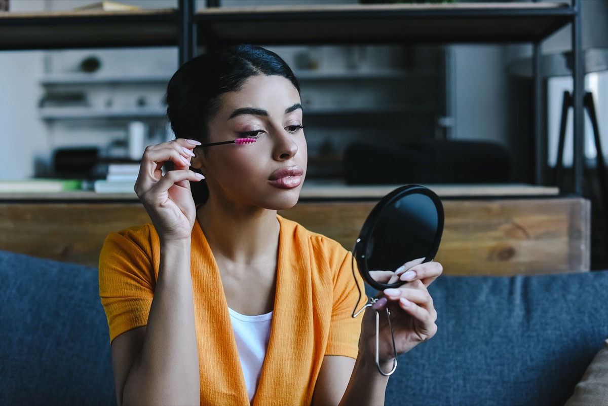 orange shirt applying mascara at home