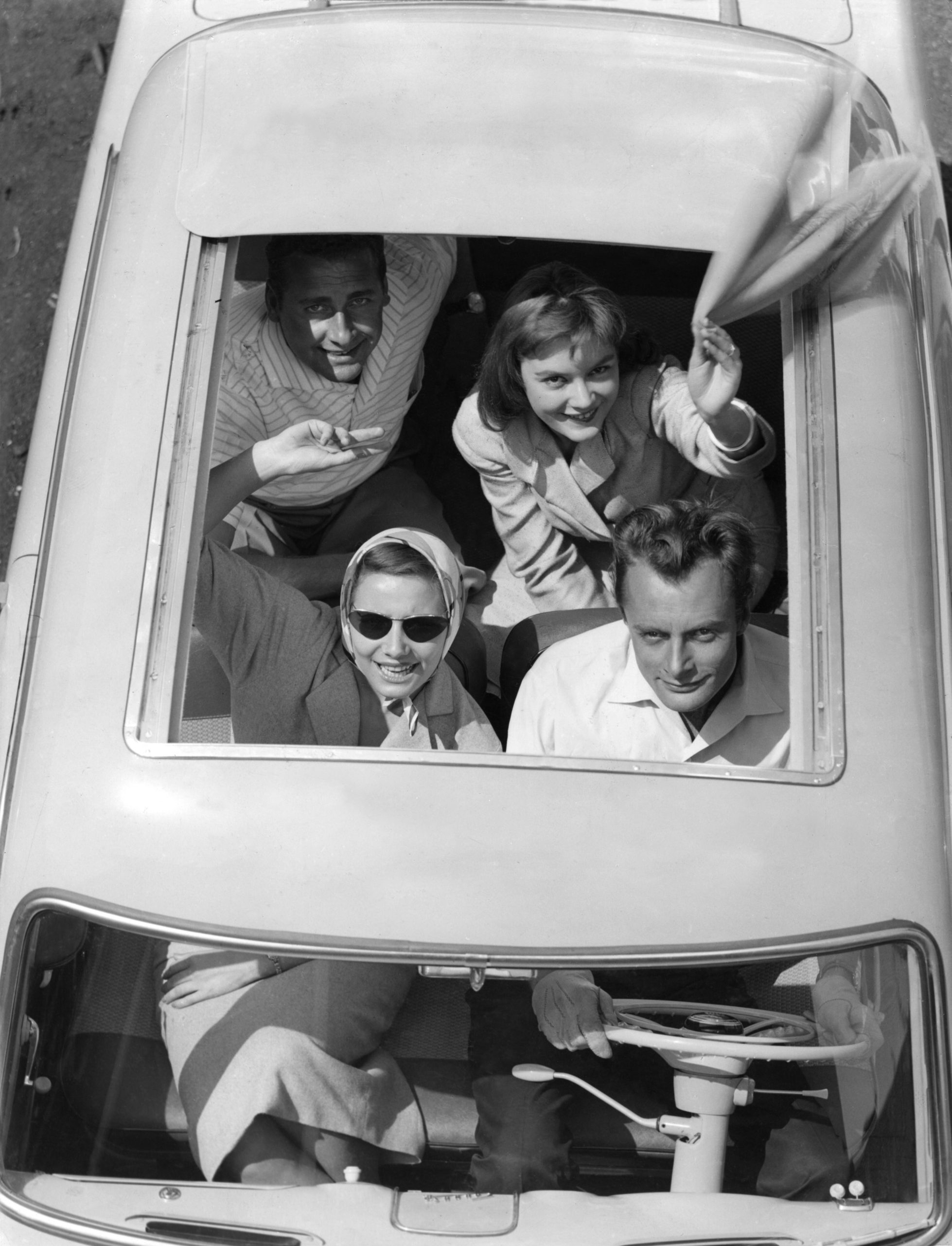 young people waving from open convertible top of car in 1950s