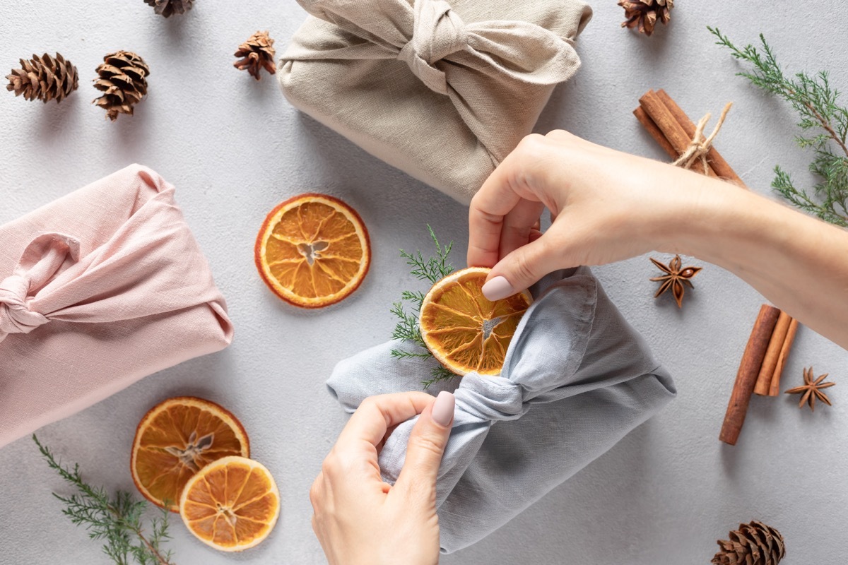 female hands packing gifts in linen cloth. Furoshiki gifts. Zero waste Christmas. top view.