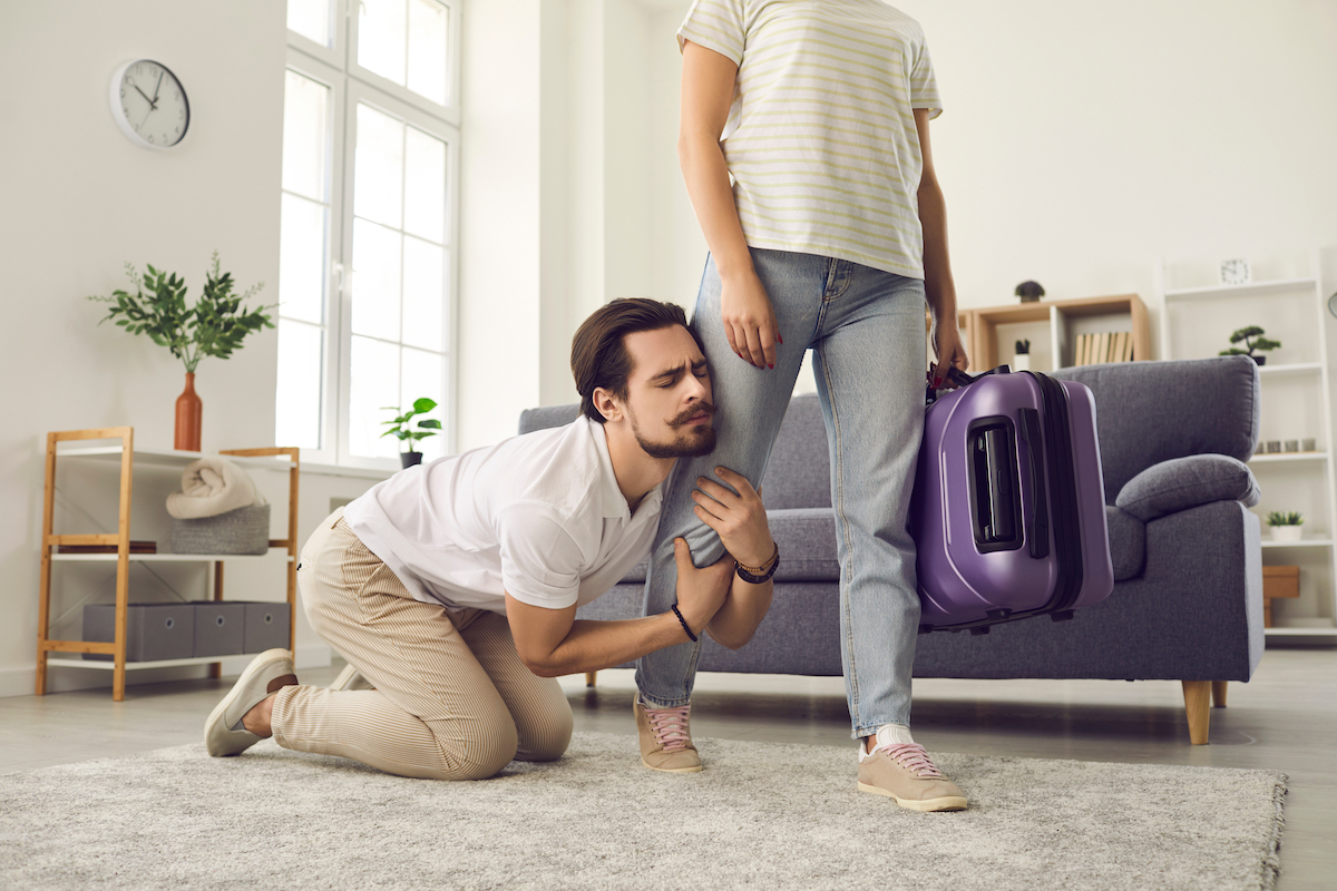 Young man clinging to woman's leg as she leaves with a suitcase.