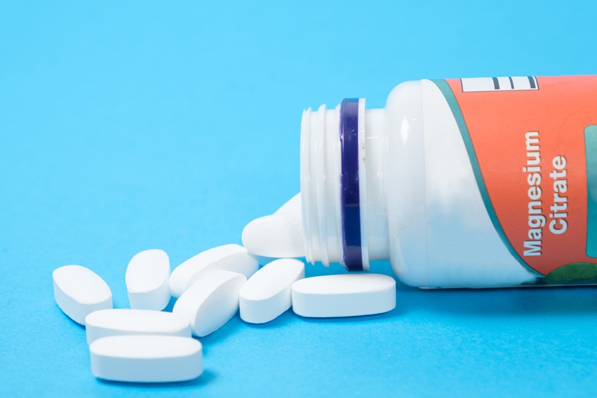 Magnesium citrate pills spill out of a jar on a blue background