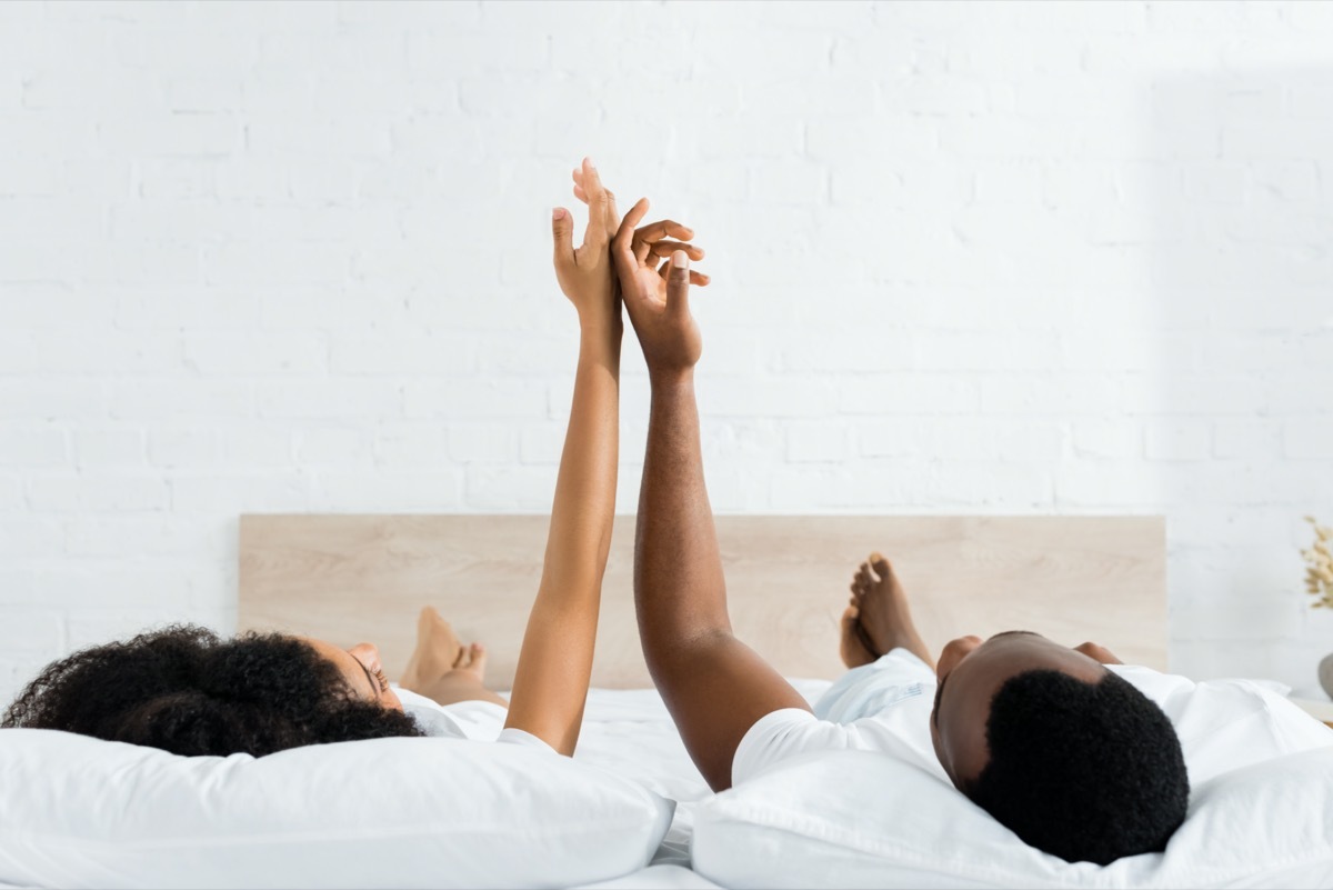 black man and woman lying on their backs in bed touching hands