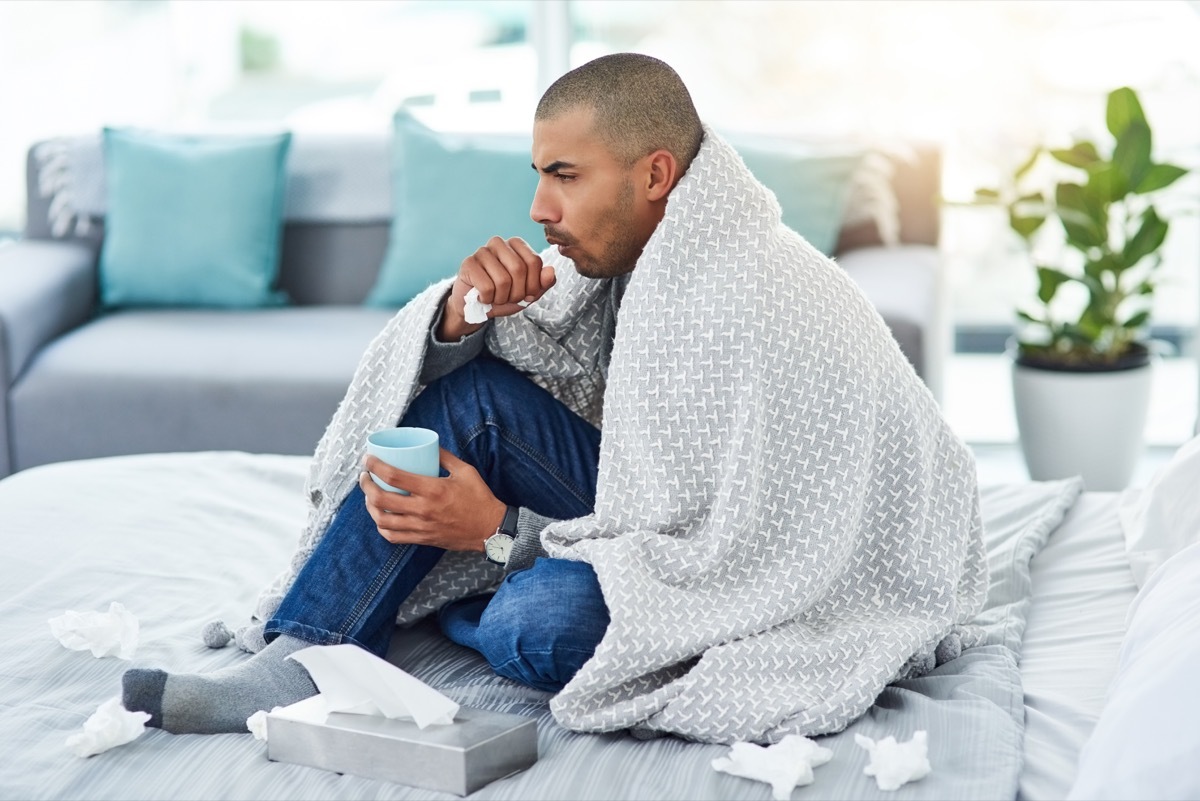 Full length shot of a young man sitting on his bed while feeling unwell at home