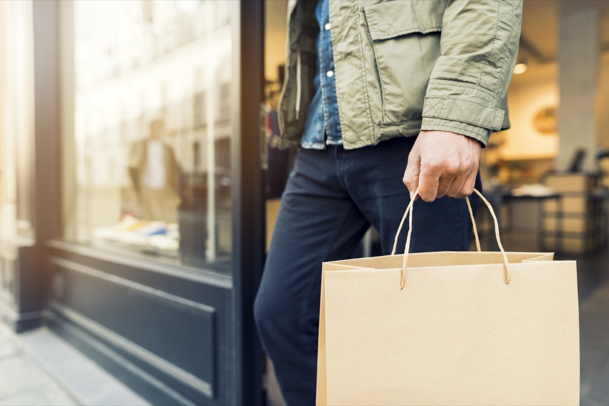 man with shopping bag walking out of store