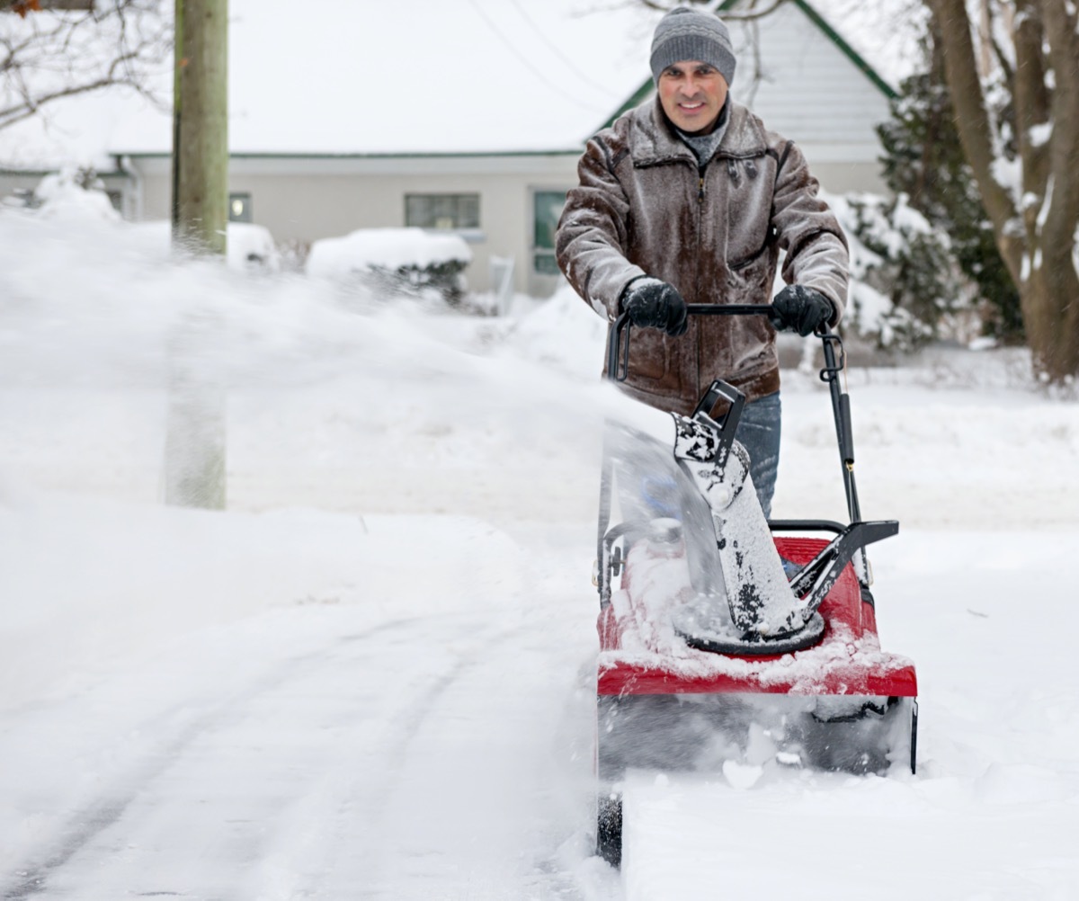 Man clearing deep snow from residential driveway after heavy snowfall