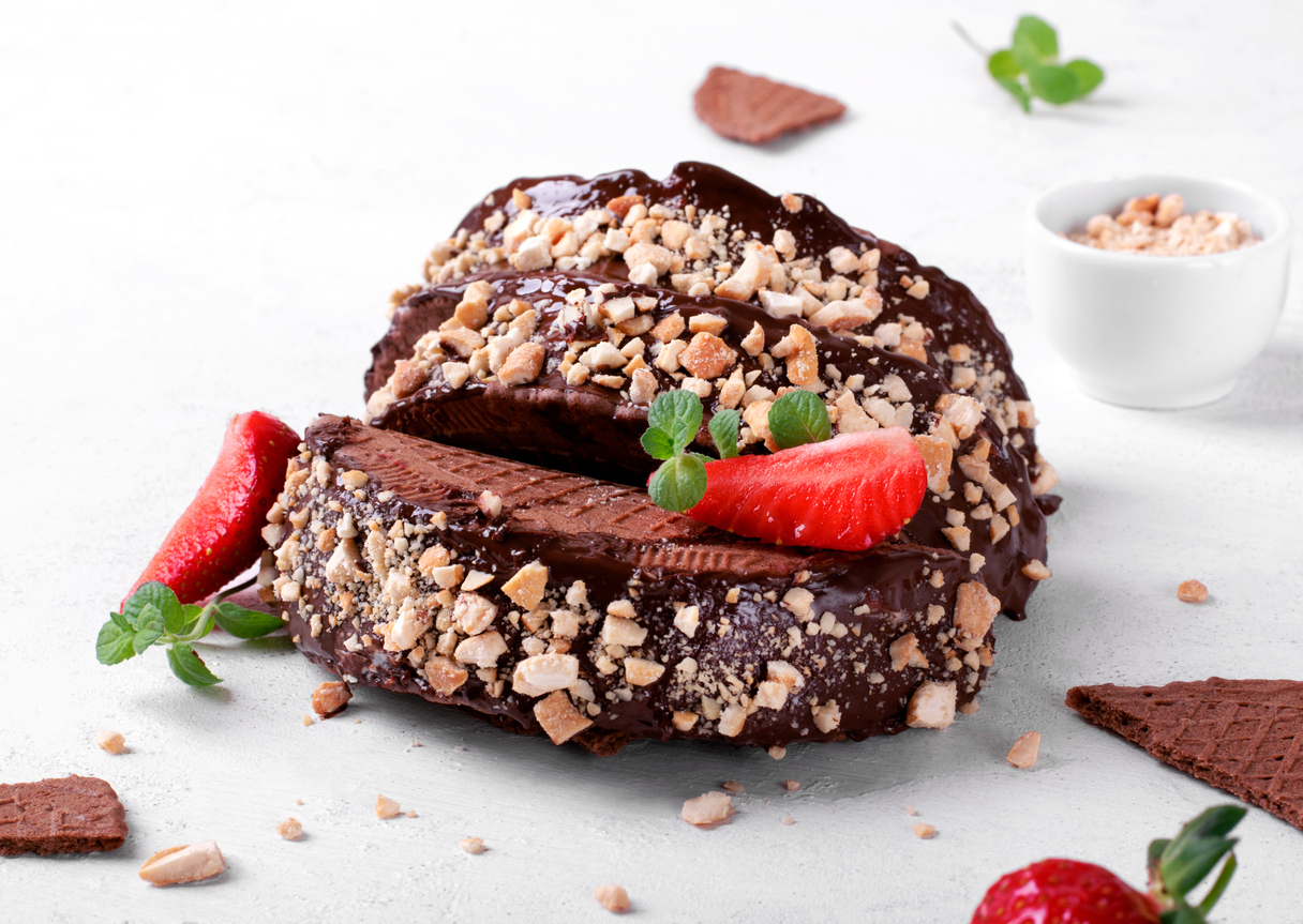 Sweet tacos with chocolate thin waffle and ice cream topped with nuts and strawberry on the white table. Dessert variation of Mexican classics