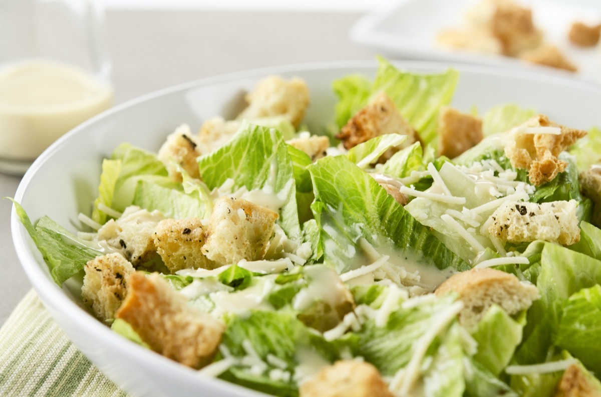 Closeup of a fresh caesar salad, with romaine lettuce hearts, croutons, parmesan cheese and dressing. Dressing and croutons in background. Very shallow DOF.