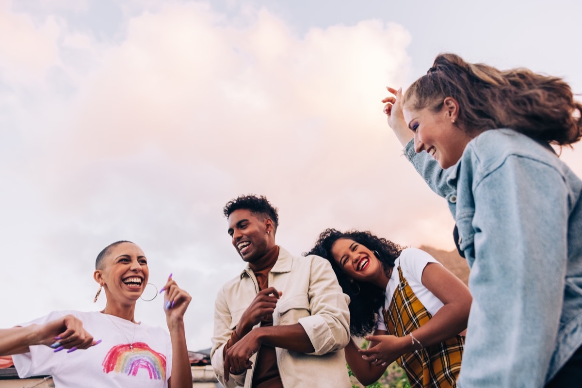 Four multicultural friends dancing on the rooftop. Group of happy young friends laughing and having a good time during a party. Vibrant young people having fun together on the weekend.