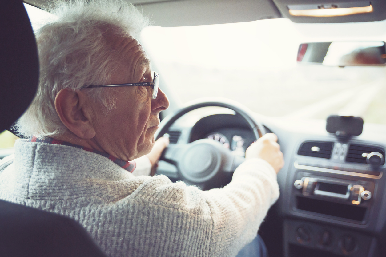 A senior man wearing glasses sitting behind the wheel of a car