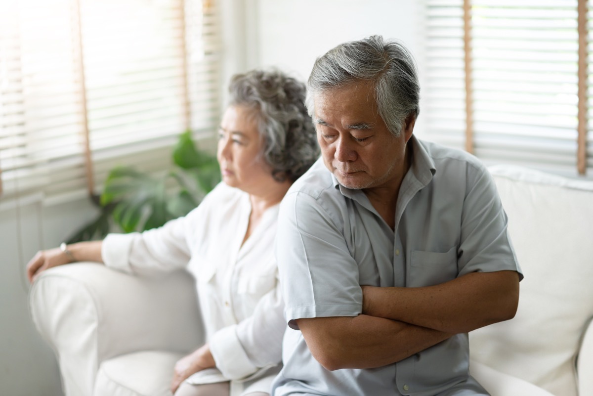 older asian couple sitting on couch looking upset and angry