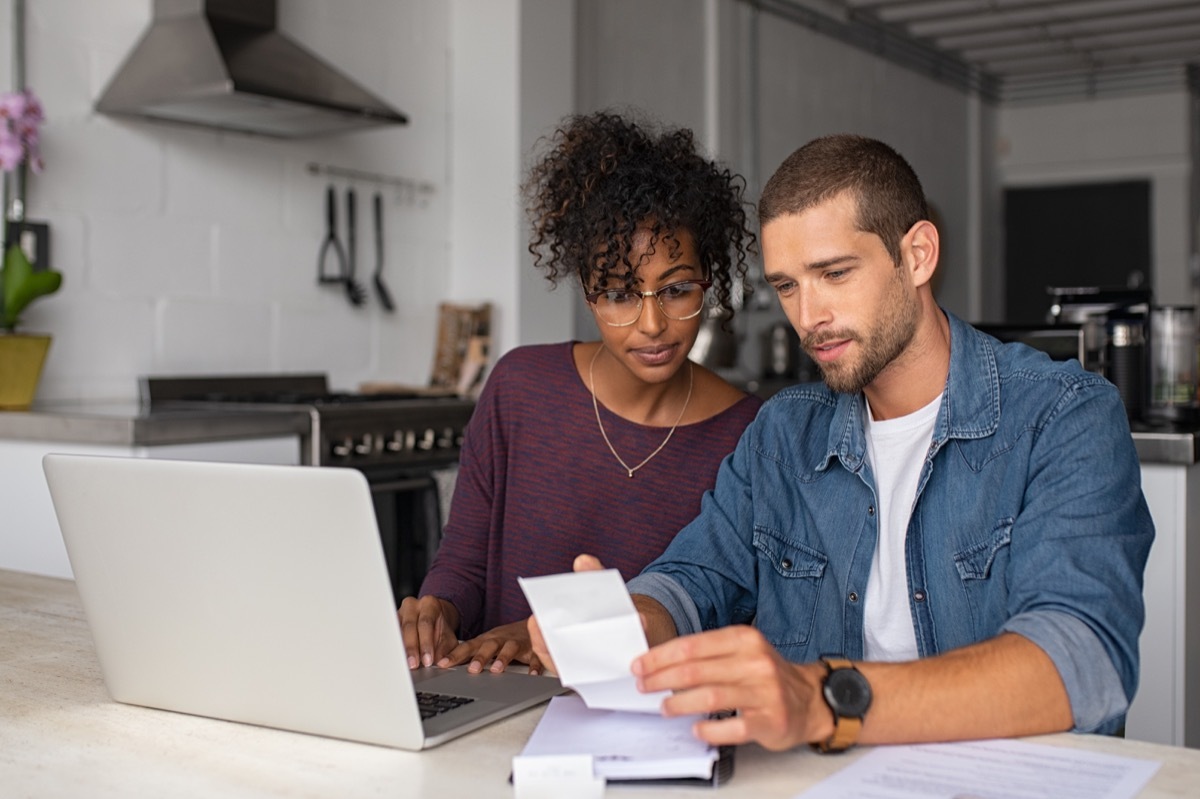 couple checking bills while managing accounts on home banking sitting at home discussing finance for the month