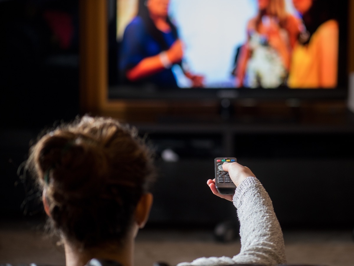 young girl watching TV with remote control in living home