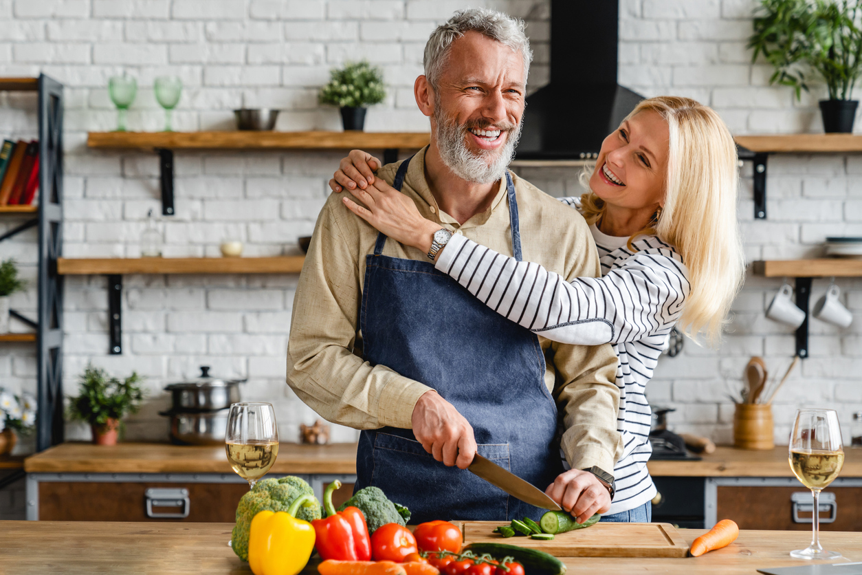 A senior couple hugging while they cook a meal in the kitchen