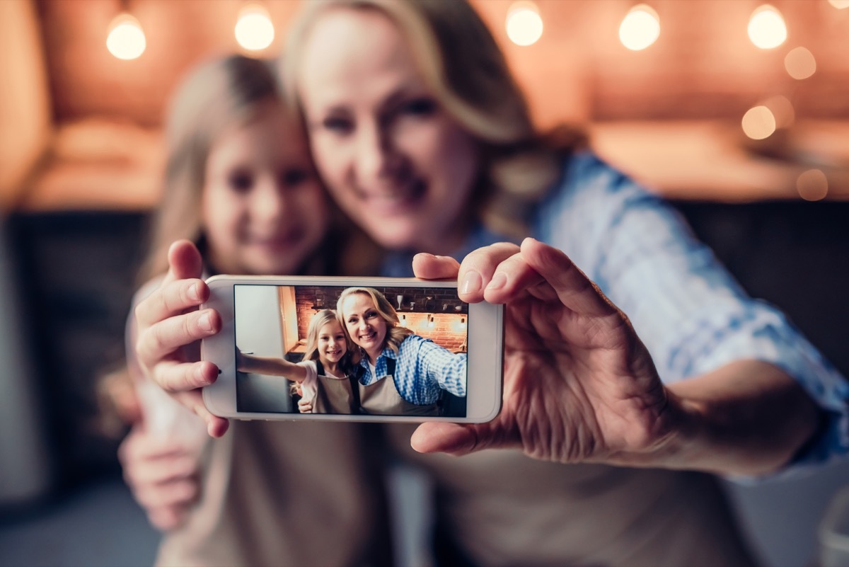 Grandmother and granddaughter are making selfie on a smart phone while cooking on kitchen.