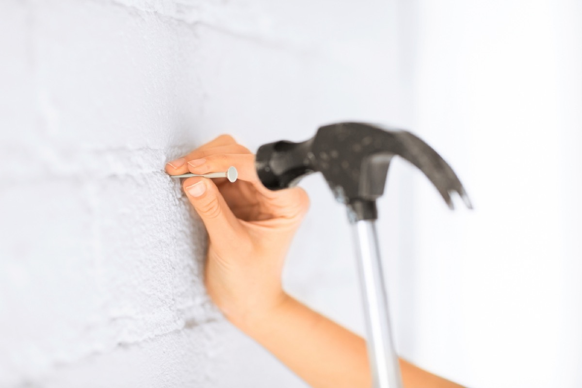 woman hammering nail into white brick wall