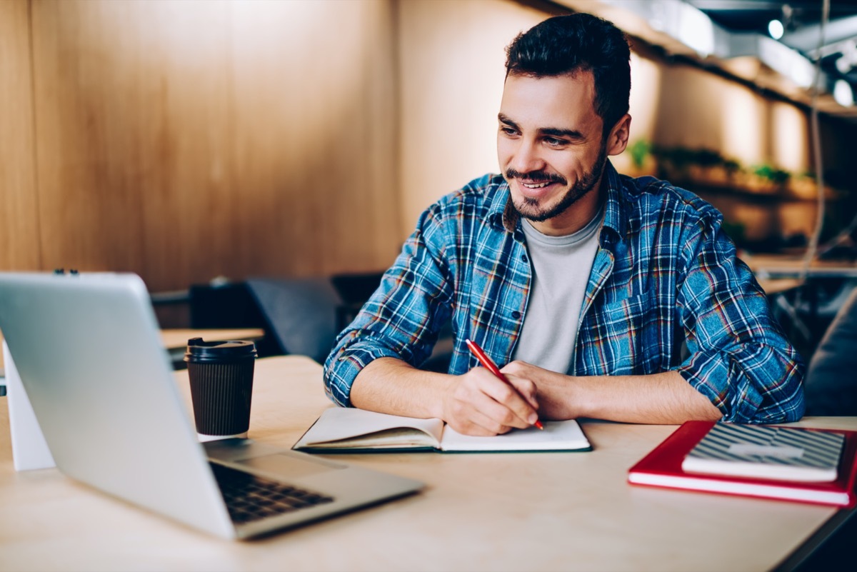 Young hispanic man studying with laptop and notebook