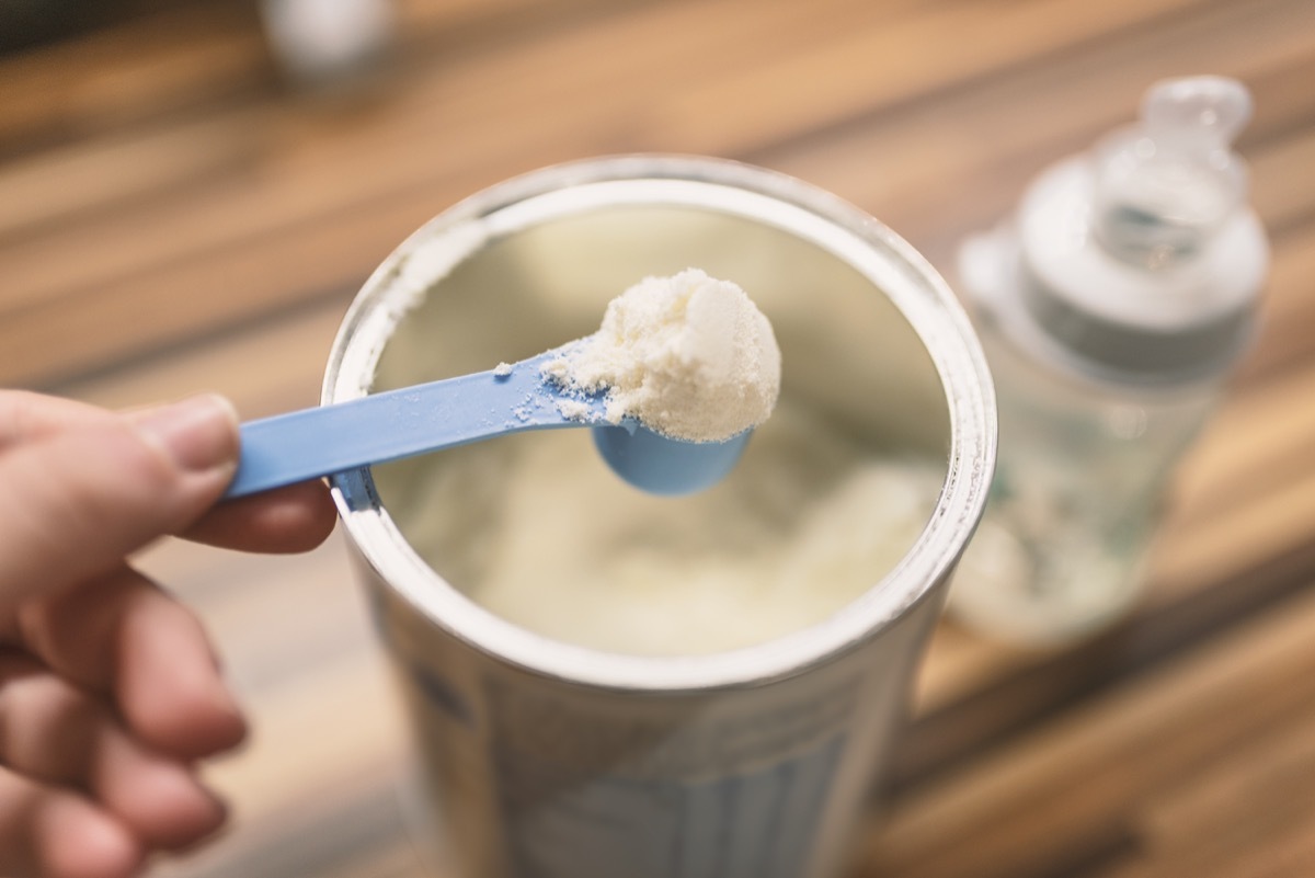 Powder milk for baby and blue spoon on light background close-up. Milk powder for baby in measuring spoon on can. Powdered milk with spoon for baby. Baby Milk Formula and Baby Bottles. Baby milk formula on kitchen background