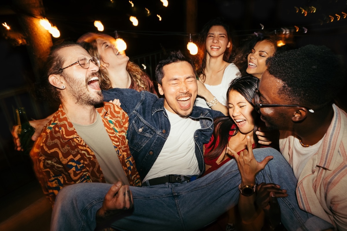 group of people carrying their friend while laughing