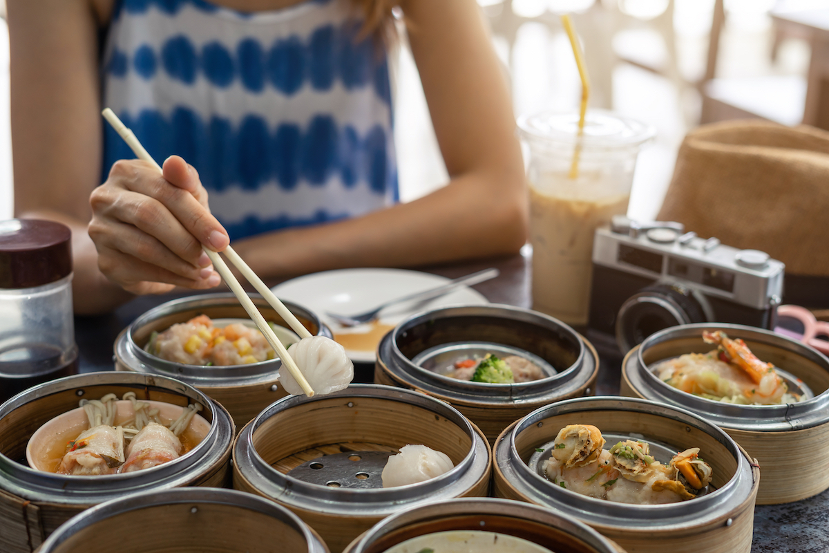 Close-up of a woman's hands using chopsticks to eat dim sum.