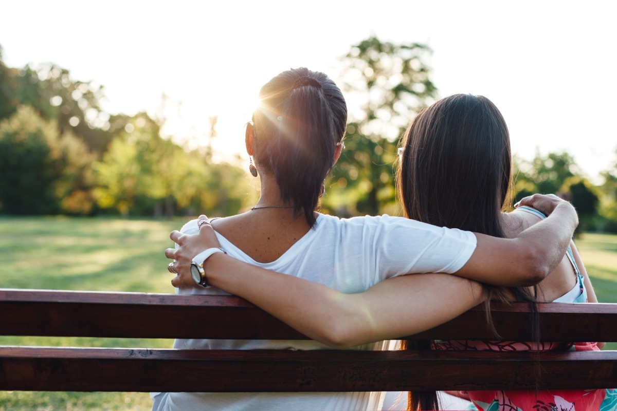 Mom and daughter sit on park bench looking at sunset, pregnant teen