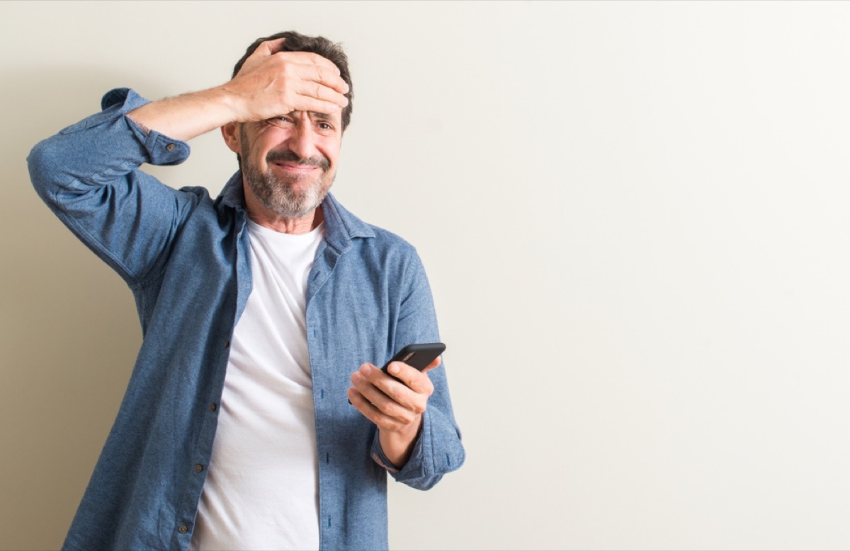 middle aged man using smartphone stressed with hand on head